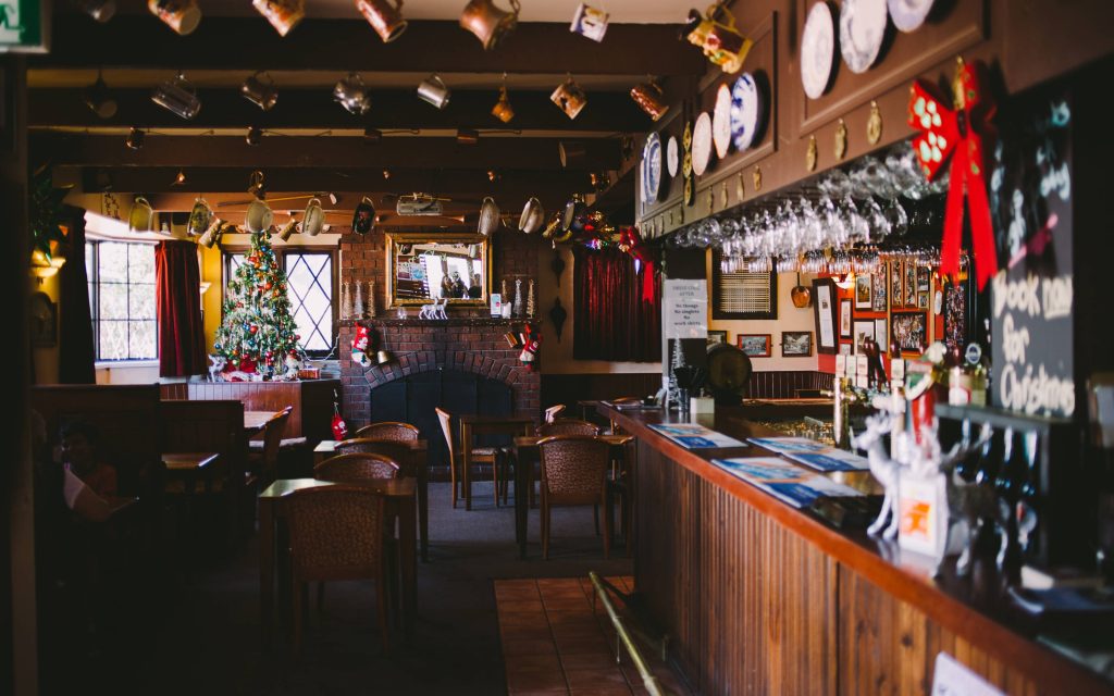 Cozy festive pub interior with Christmas tree stockings brick fireplace and hanging mugs wallpaper