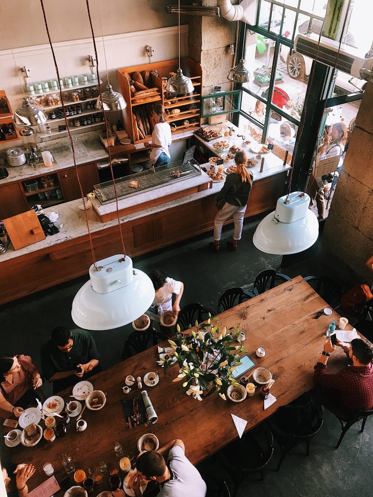 High-angle view of bustling rustic coffee shop with communal table industrial lighting and pastries Wallpaper