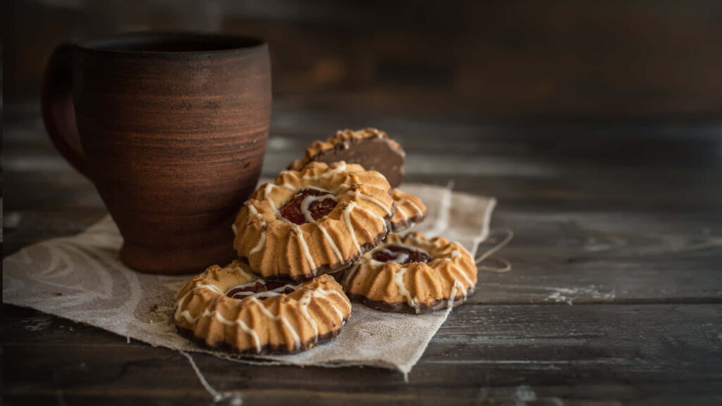 Rustic brown mug with berry jam cookies on linen cloth wooden table cozy wallpaper background