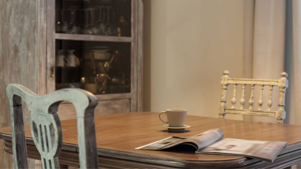 Cozy rustic wooden dining table with open magazine coffee cup vintage chairs warm lighting Wallpaper