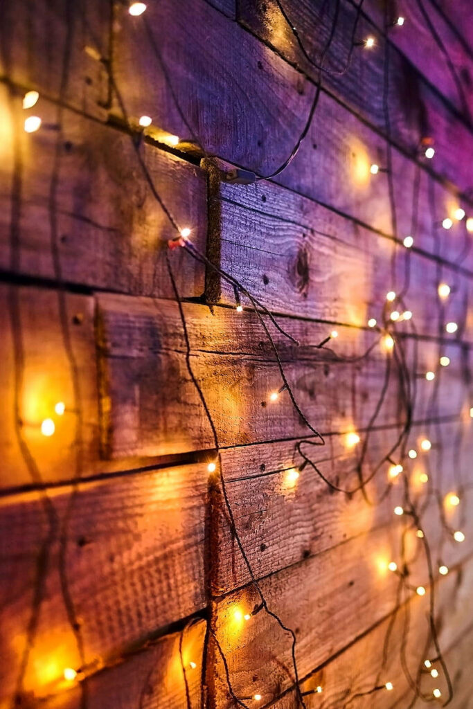 Cozy warm string lights draped on rustic wooden planks creating enchanting wallpaper background
