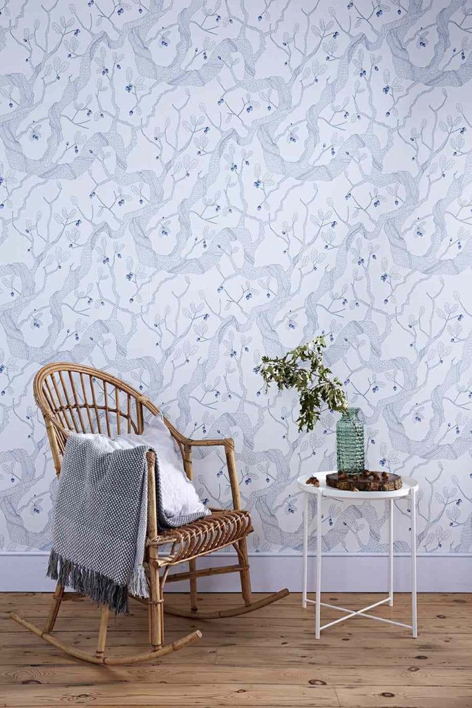 Cozy corner with rattan rocking chair textured throw white side table green vase botanical wallpaper