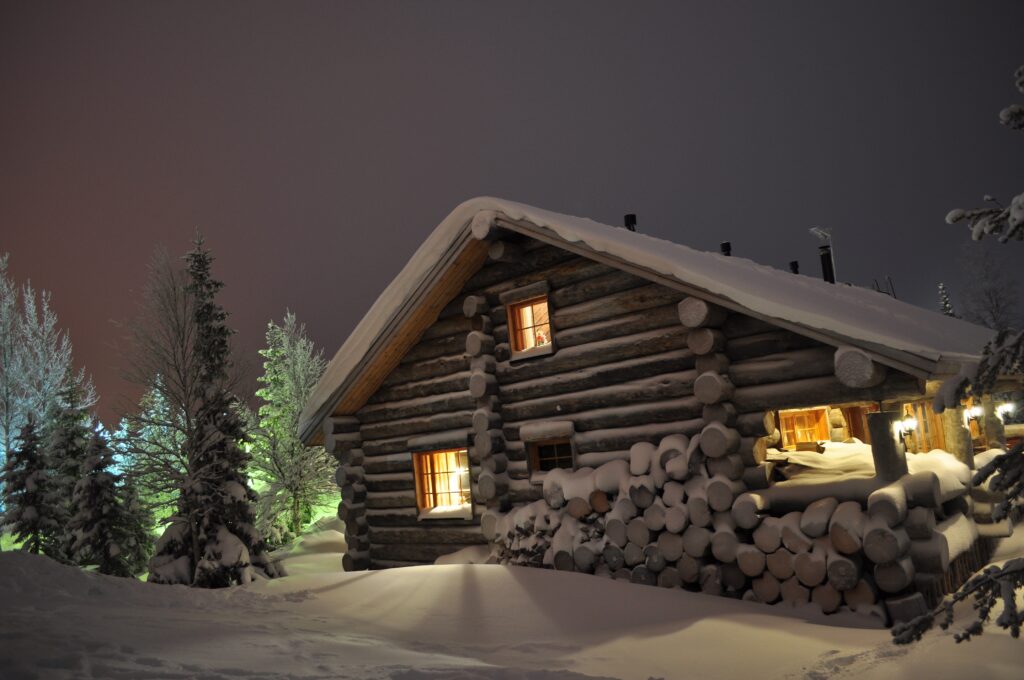 Cozy log cabin glowing warmly in snowy winter landscape with tall trees under night sky Wallpaper