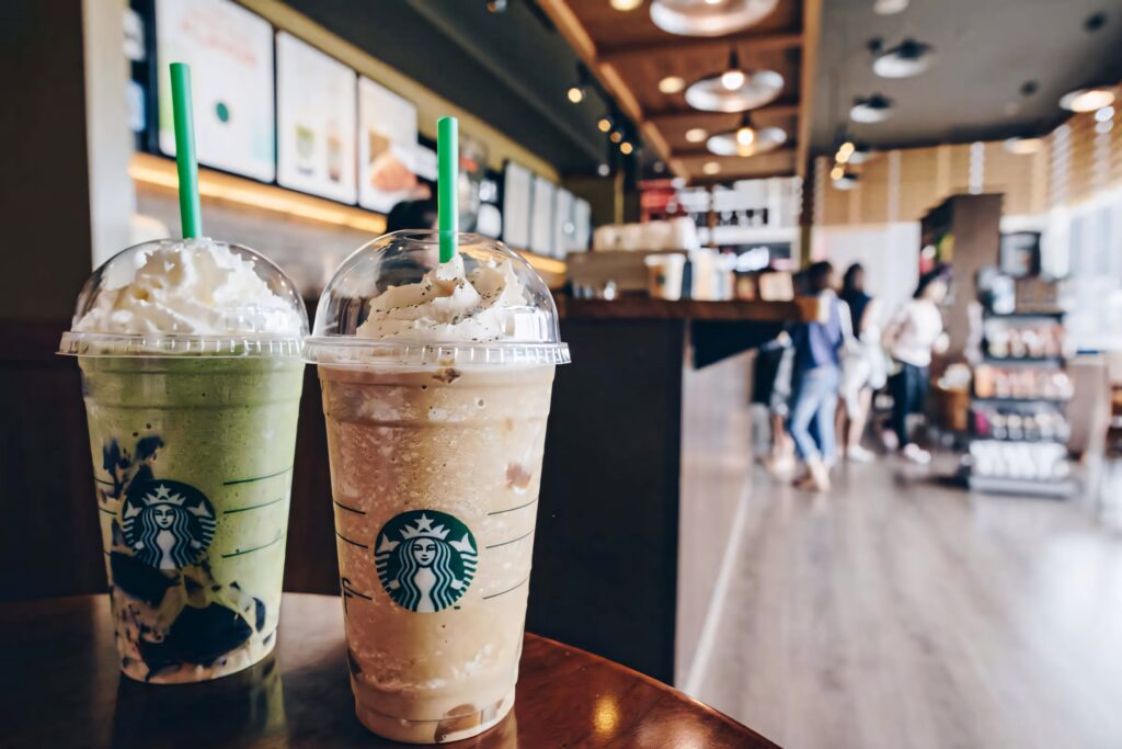 Two Starbucks drinks with whipped cream in a cozy café setting wallpaper background