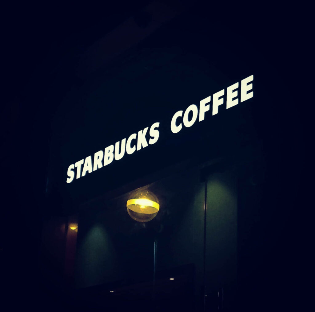 Glowing Starbucks Coffee LED sign on dark background creating cozy inviting cafe atmosphere Wallpaper