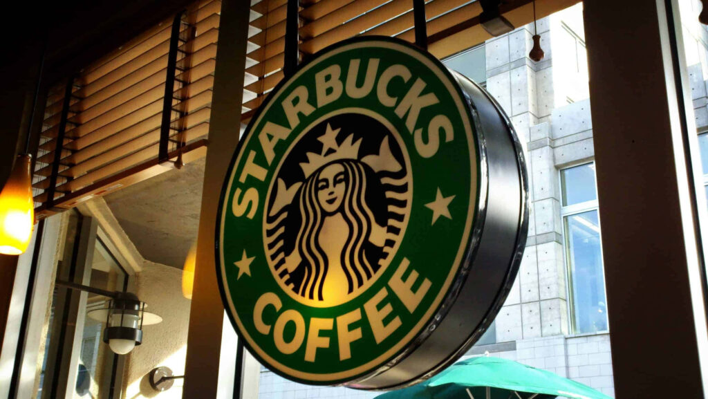 Bright Starbucks Coffee sign glowing in cozy shop setting for perfect morning vibe wallpaper