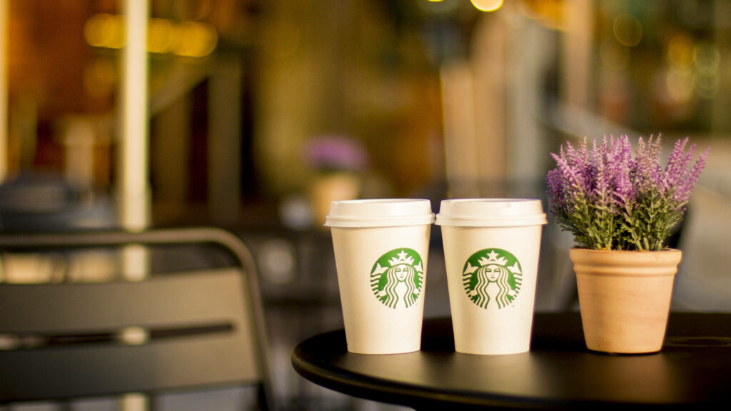 Cozy Starbucks scene with two cups and a lavender plant on café table background wallpaper