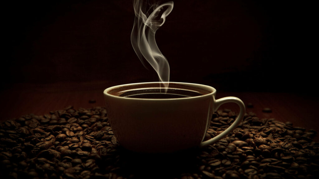 Steaming hot coffee cup surrounded by roasted beans on dark background cozy morning vibe Wallpaper