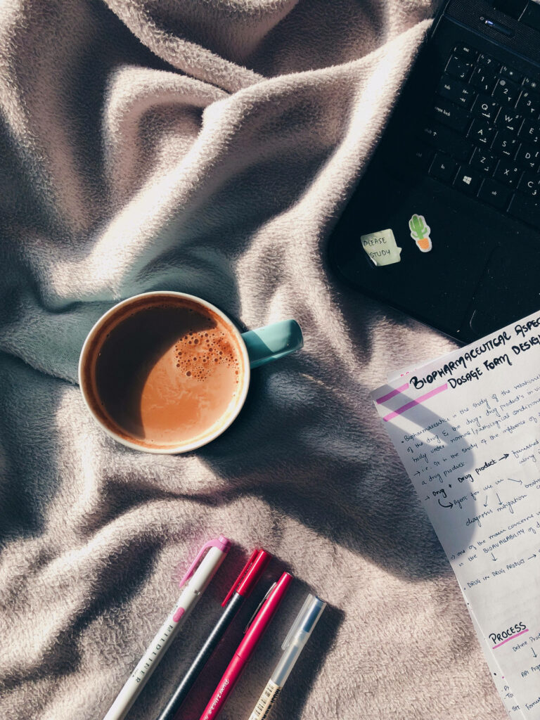 Cozy study workspace with sunlight soft blanket coffee laptop colorful pens and handwritten notes Wallpaper