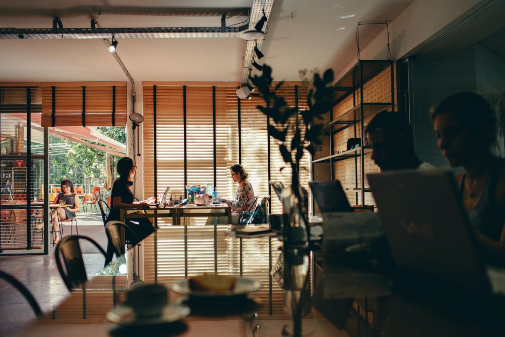 Cozy coffee shop interior with warm sunlight through wooden blinds creating calm workspace ambiance Wallpaper