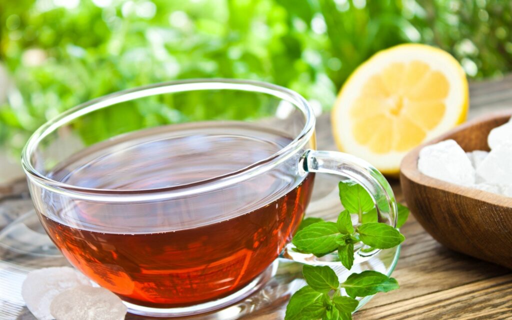 Cozy Tea Scene: Glass Cup, Lemon, Mint & Sugar on Wooden Table Wallpaper