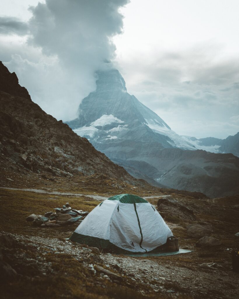 Cozy tent among rugged rocks at snowcapped mountains base with mist and soft natural light Wallpaper