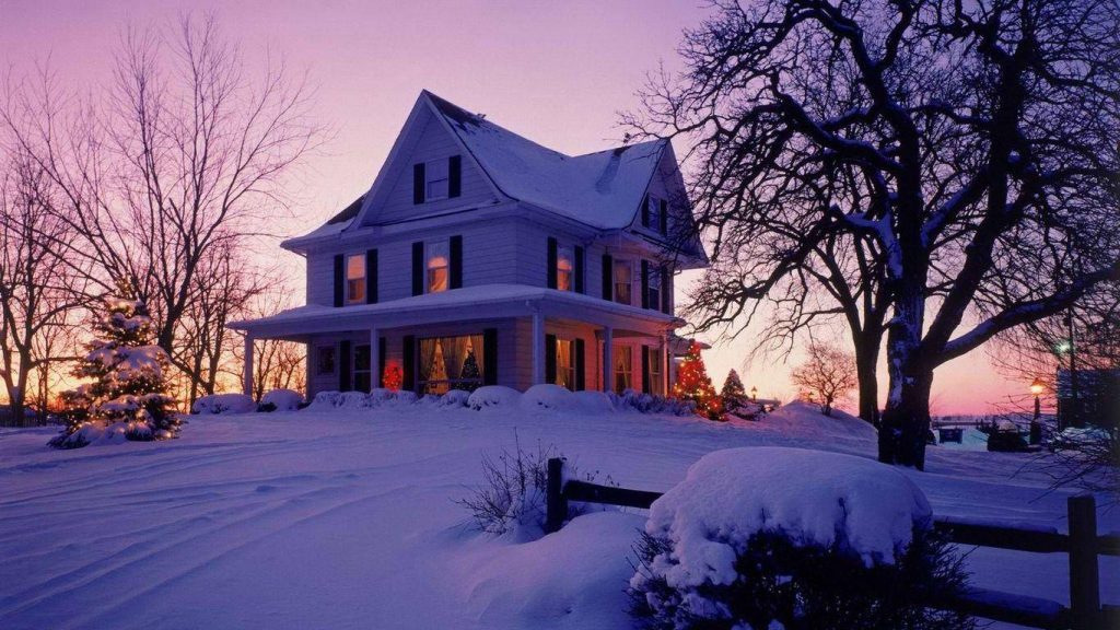 Snow-covered Victorian house at twilight with warm windows and festive tree sunset background Wallpaper