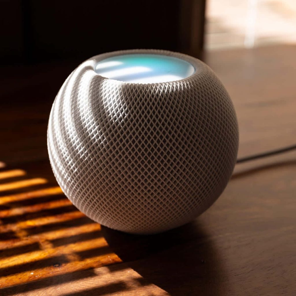 White Apple HomePod mini on wooden table with warm sunlight and striped shadows wallpaper