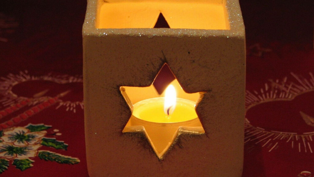 Warm yellow candle glowing in textured cream box with star cutout on festive red background Wallpaper