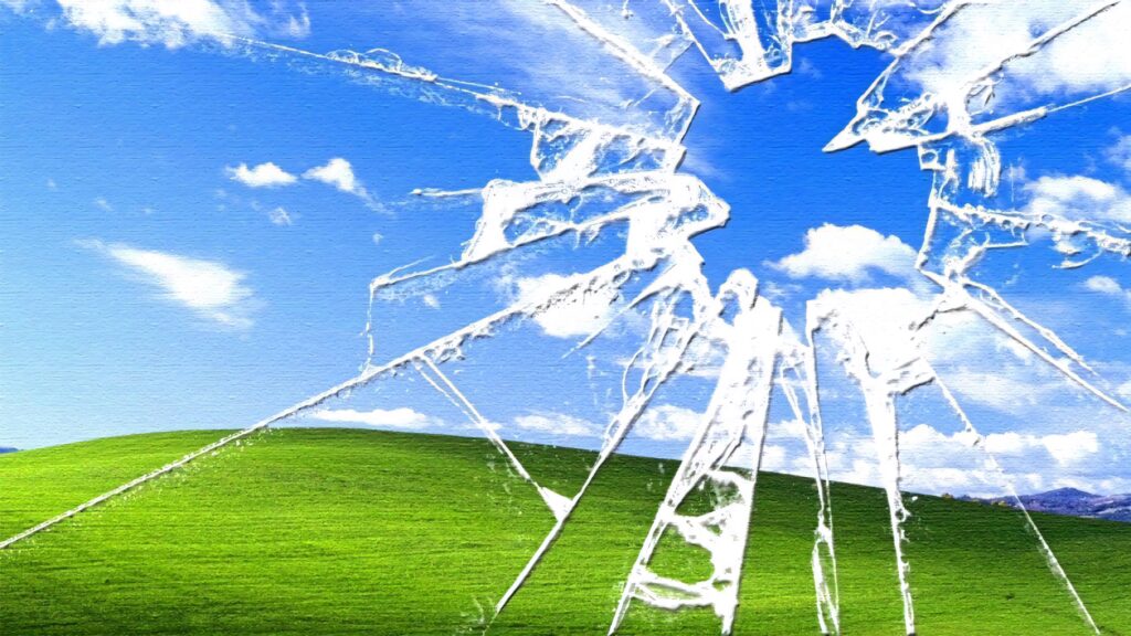 Cracked computer screen showing classic Windows Bliss green hills and blue sky wallpaper background