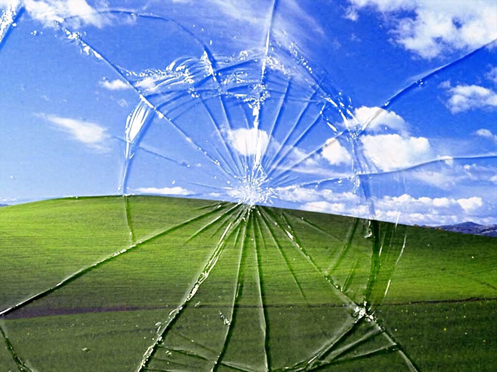 Cracked computer screen with iconic rolling green hills and blue sky Bliss wallpaper background