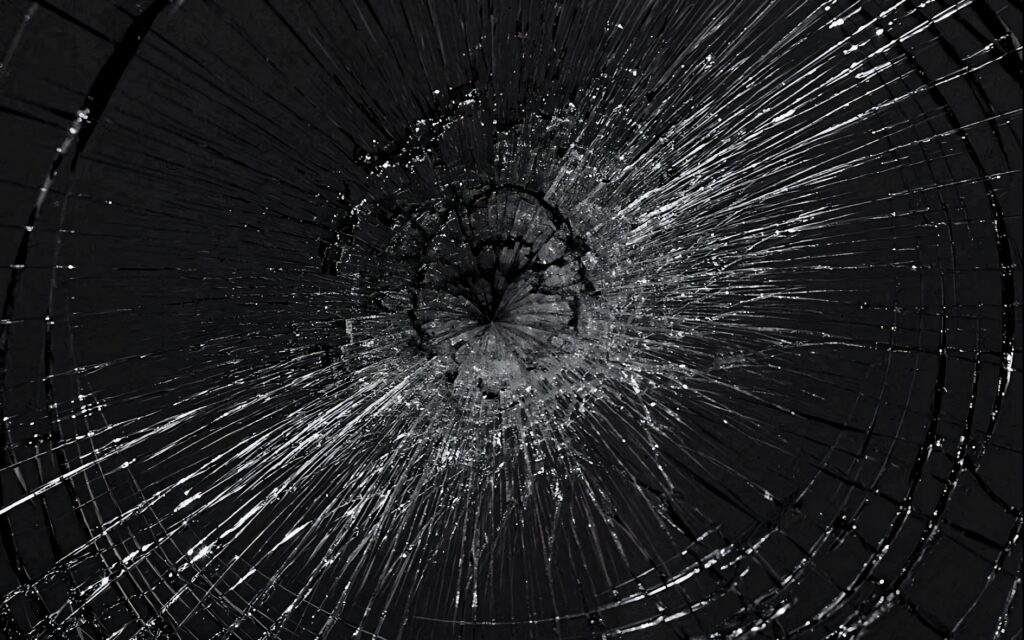 Close-up of shattered black and white computer screen with central bullet hole crack wallpaper background