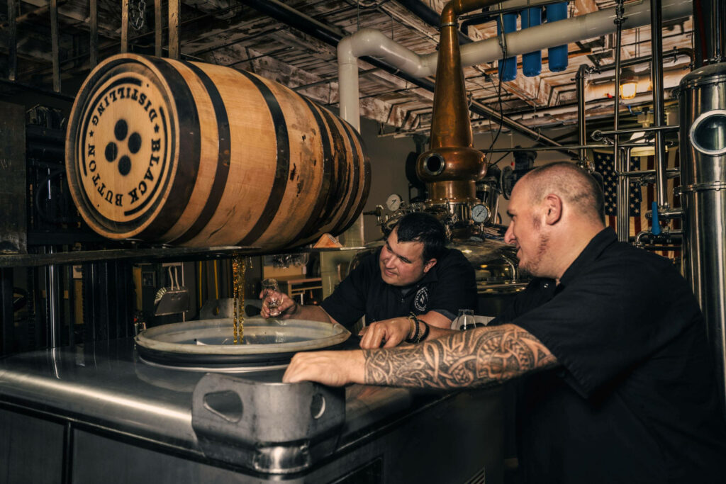 Two distillers inspecting whiskey aging barrels and copper equipment in craft distillery room Wallpaper