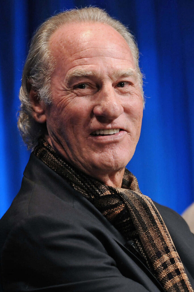 Craig T Nelson candid portrait in dark suit with patterned scarf on rich blue wallpaper background