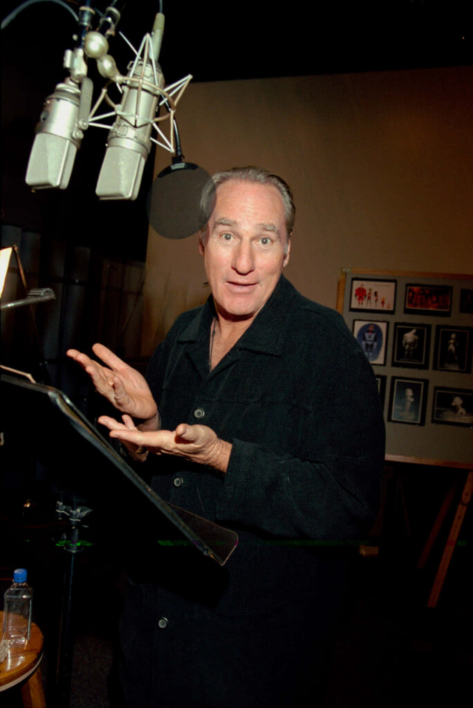 Craig T Nelson voice actor recording studio animated gestures warm lighting framed photos background Wallpaper