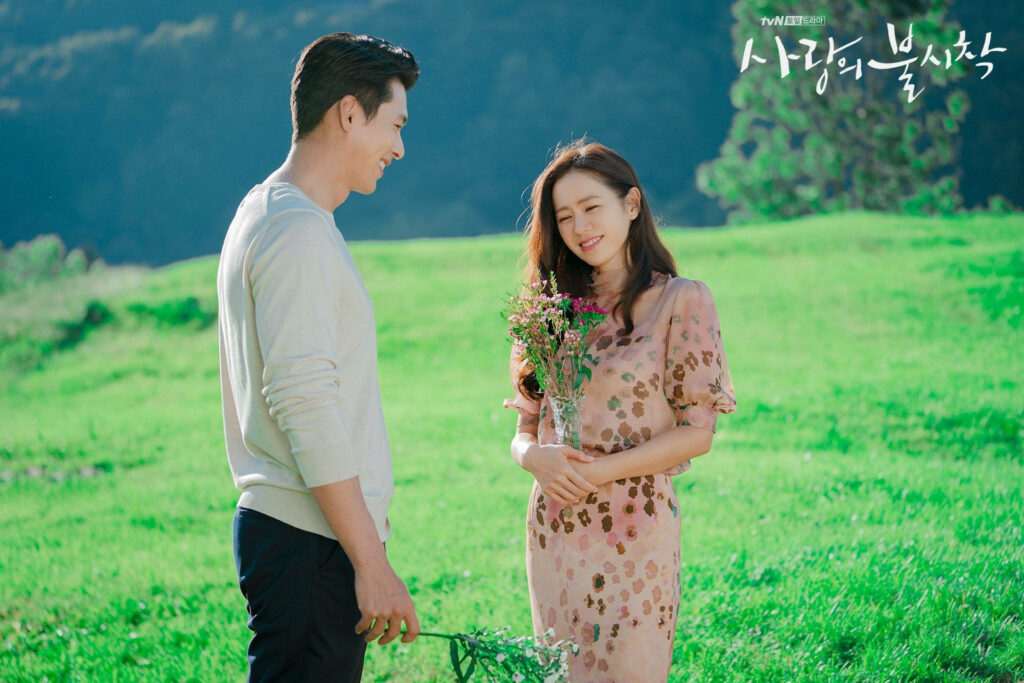 Yoon Se-ri and Ri Jeong-hyeok share a romantic moment in a sunlit green field Crash Landing On You wallpaper