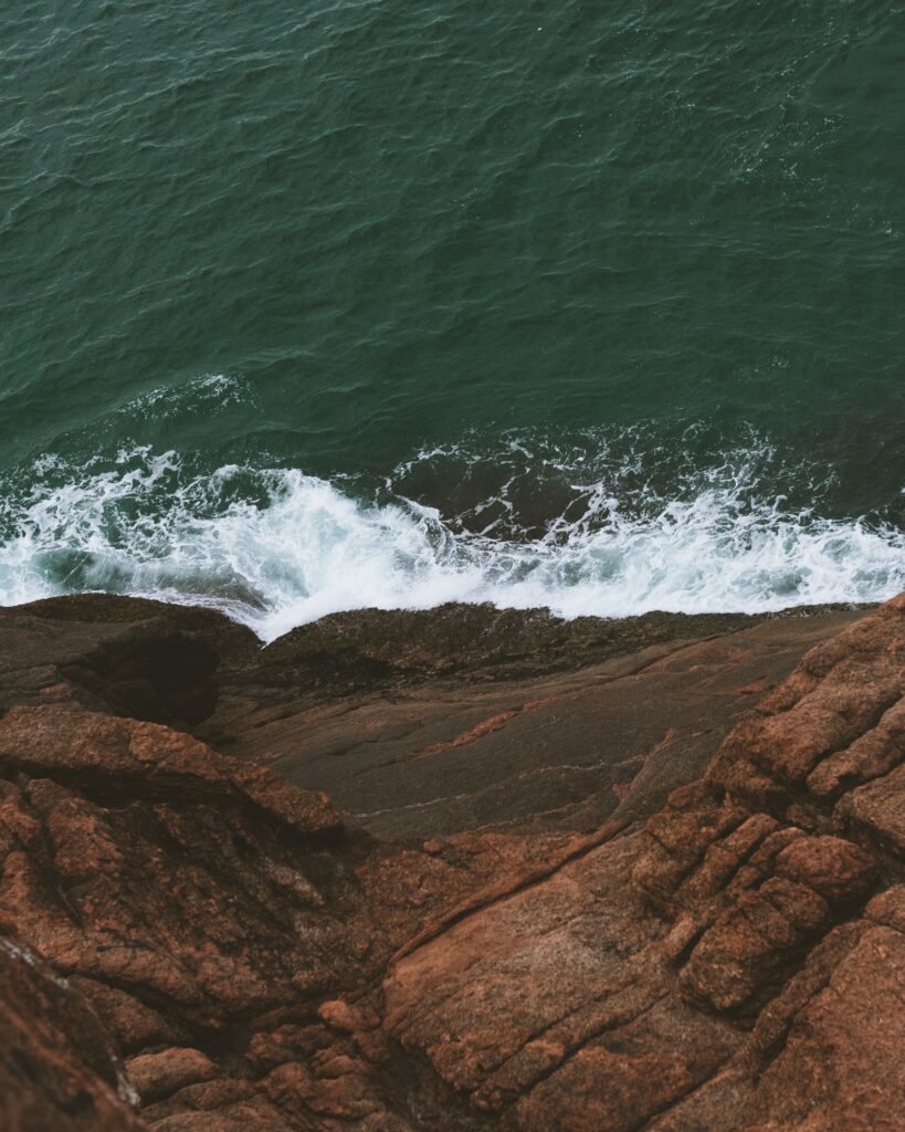 Crashing ocean waves hit rugged coastal rocks with blue green water and warm earthy tones wallpaper