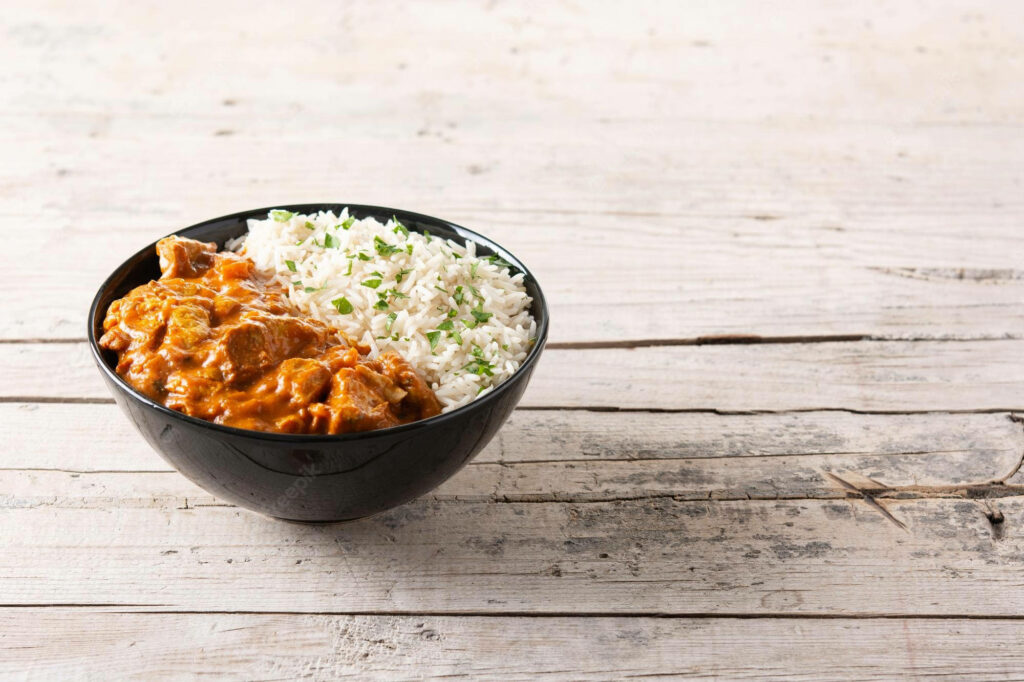 Bowl of aromatic white rice with creamy butter chicken curry on rustic wooden background Wallpaper