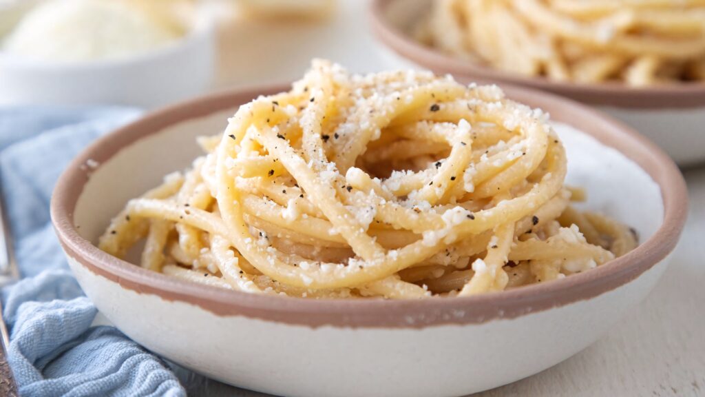 Creamy Cacio e Pepe pasta in rustic dish with cracked black pepper and grated cheese closeup Wallpaper