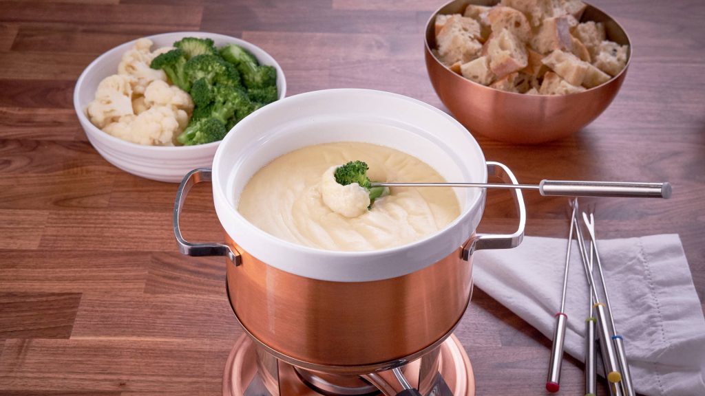Copper fondue pot with creamy cheese dip broccoli cauliflower and crusty bread on wood table Wallpaper