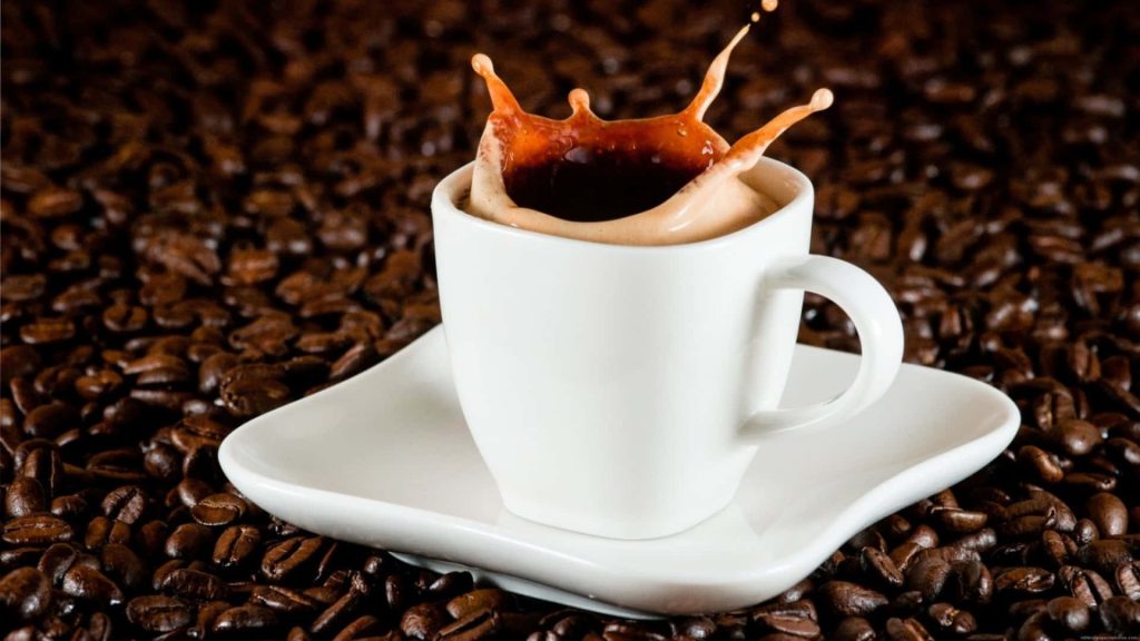 Macro photo of white ceramic coffee cup with crown splash over roasted coffee beans background Wallpaper