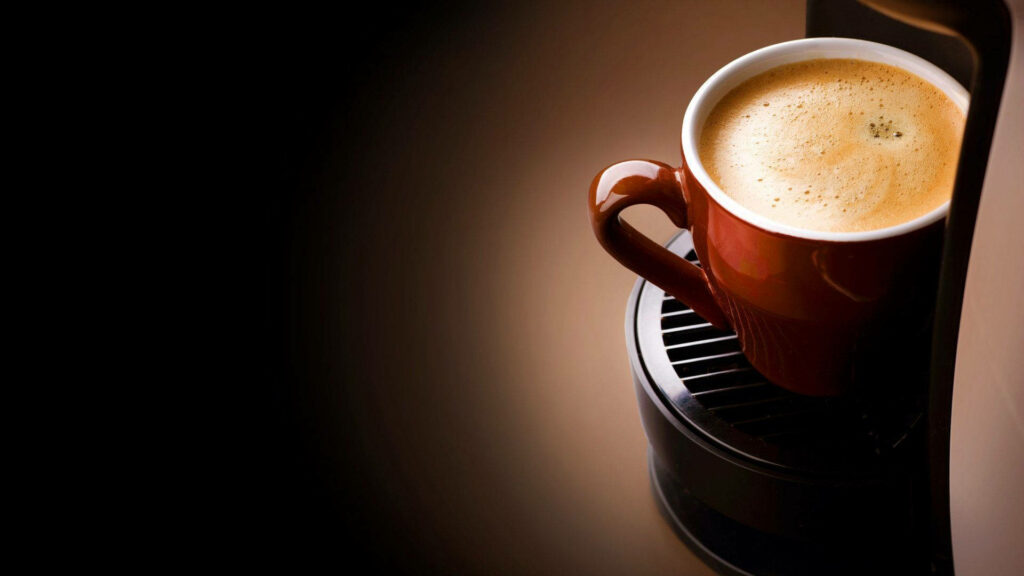 Creamy coffee in brown ceramic cup on modern coffee machine with smooth frothy layer background Wallpaper