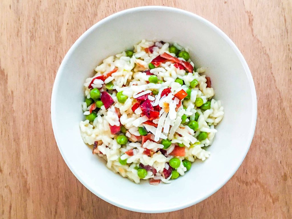 Top-down view of creamy ham and peas risotto with shredded cheese on wooden background Wallpaper