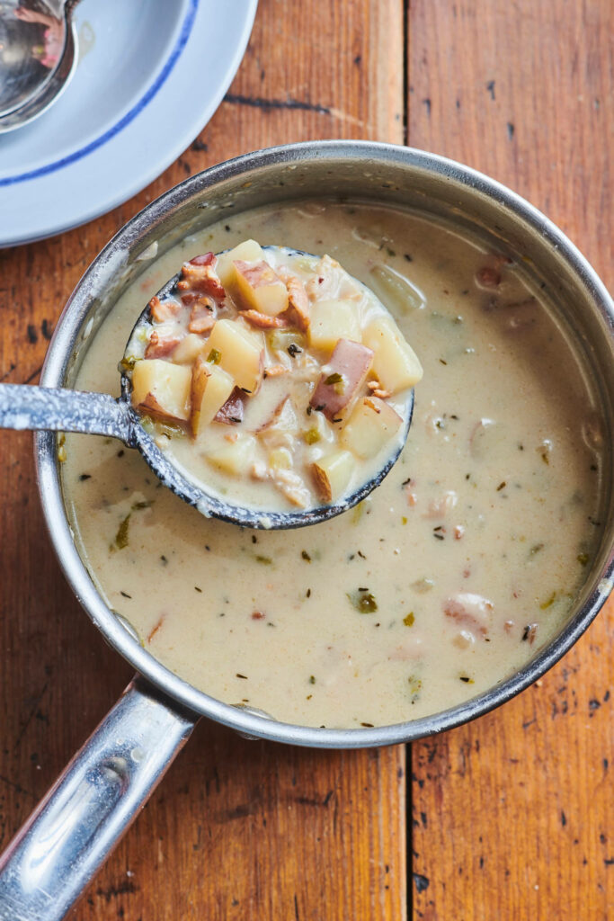 Creamy instant clam chowder with potato and herbs in pot on rustic wooden table background Wallpaper