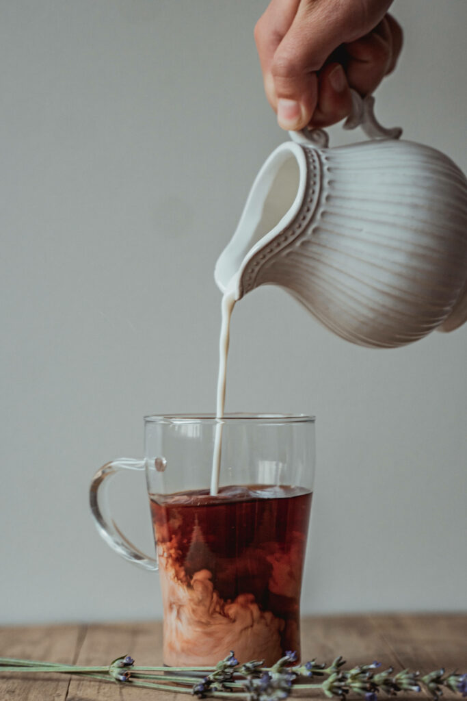 Hand pouring creamy milk from white pitcher into coffee mug creating swirling brown patterns Wallpaper