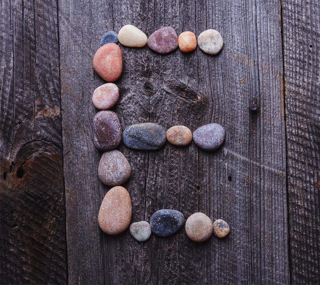 Letter E made of colorful river stones on rustic dark wooden planks natural textured wallpaper
