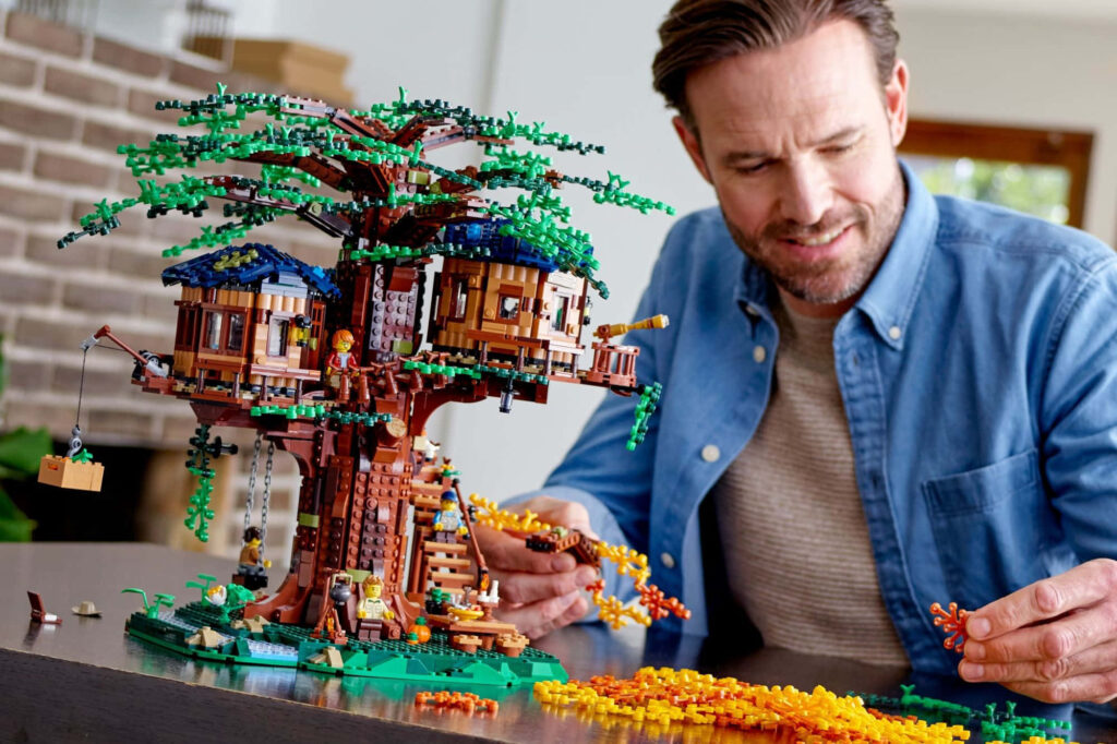 Man assembling intricate colorful LEGO treehouse set with detailed miniature pieces on wallpaper