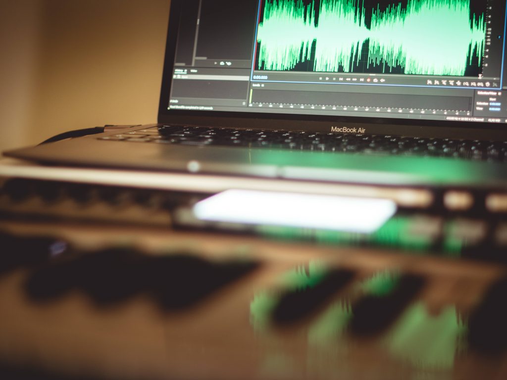 MacBook Air with vibrant green audio waveform and blurred MIDI controller music production wallpaper