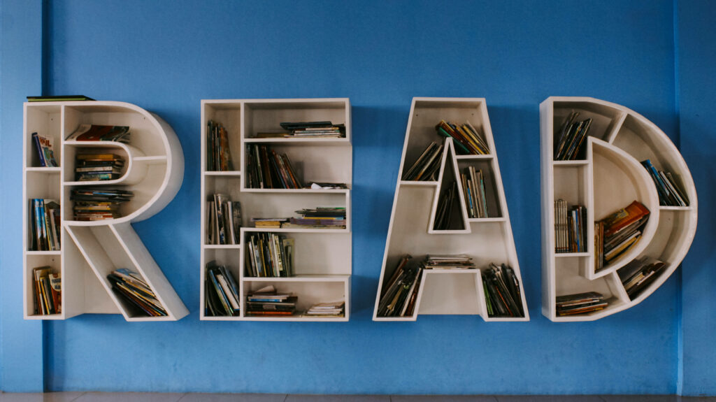 Bookshelves shaped as READ filled with colorful books on blue wall inspiring reading love Wallpaper