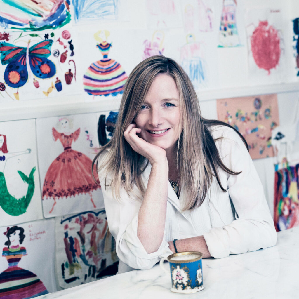 Cheerful woman at marble table in creative workspace with vibrant children's fashion drawings wallpaper