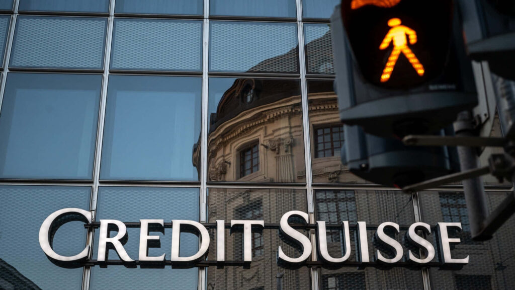 Credit Suisse logo on glass building facade with historic reflection and illuminated pedestrian signal Wallpaper