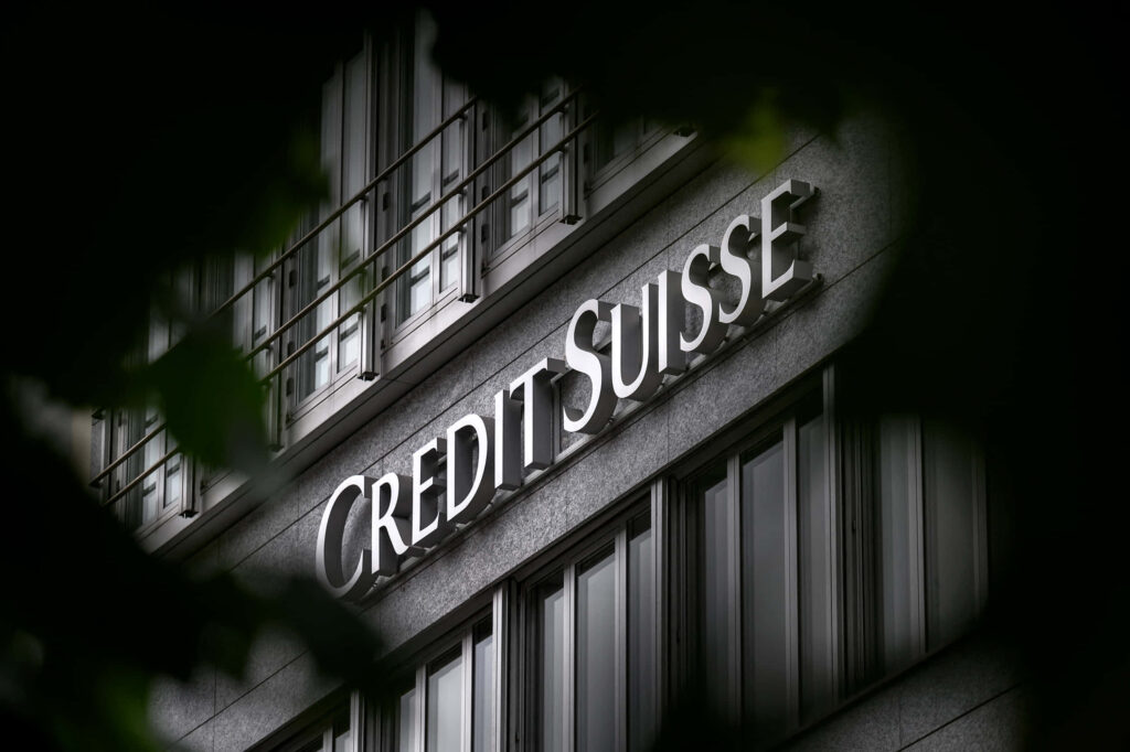 Credit Suisse logo on modern grey building with blurred green foliage financial institution facade Wallpaper