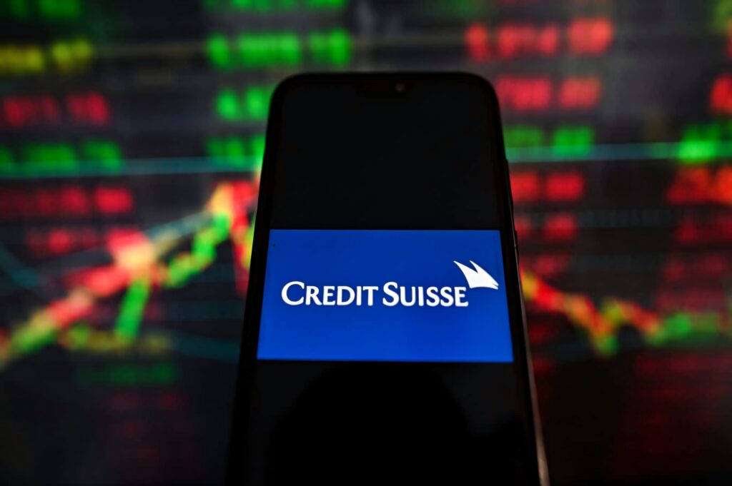 Credit Suisse logo on smartphone with blurred red green stock market graphs dark financial wallpaper