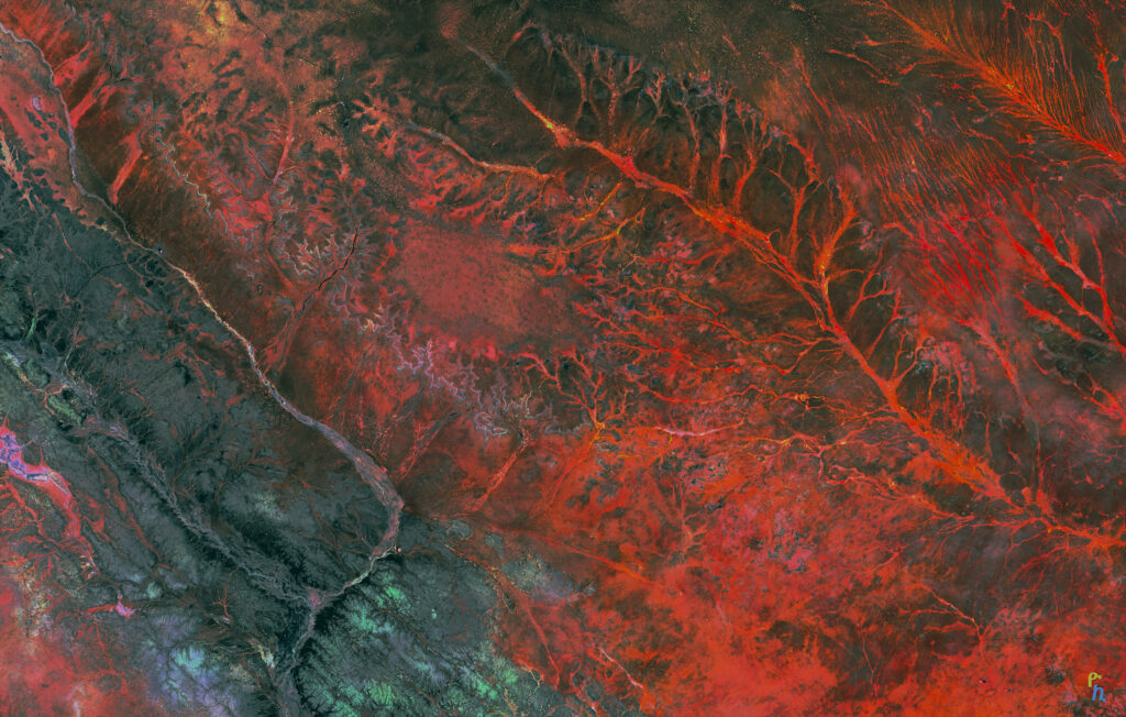 Aerial view of rugged landscape with vivid red tones and intricate natural relief patterns wallpaper