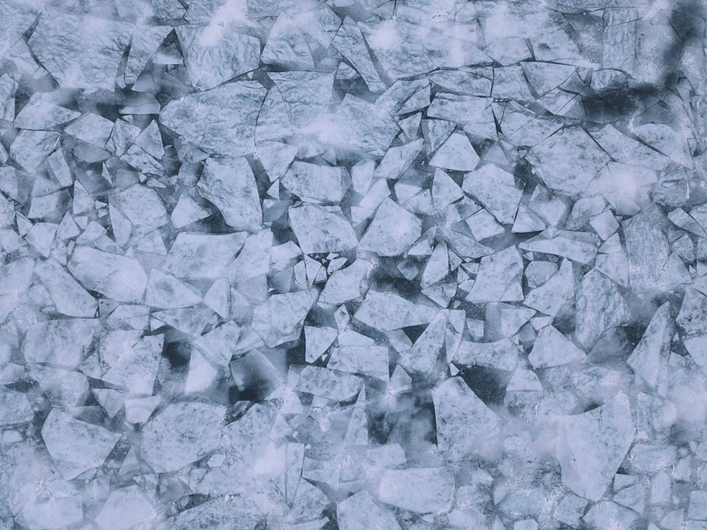 Top-down view of frozen lake ice shards mosaic in cool blue and grey tones wallpaper background