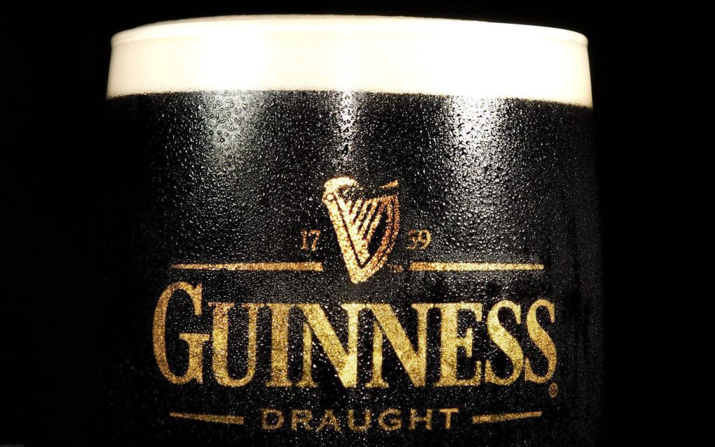 Close-up of chilled Guinness Draught pint with condensation and gold harp logo on black background Wallpaper