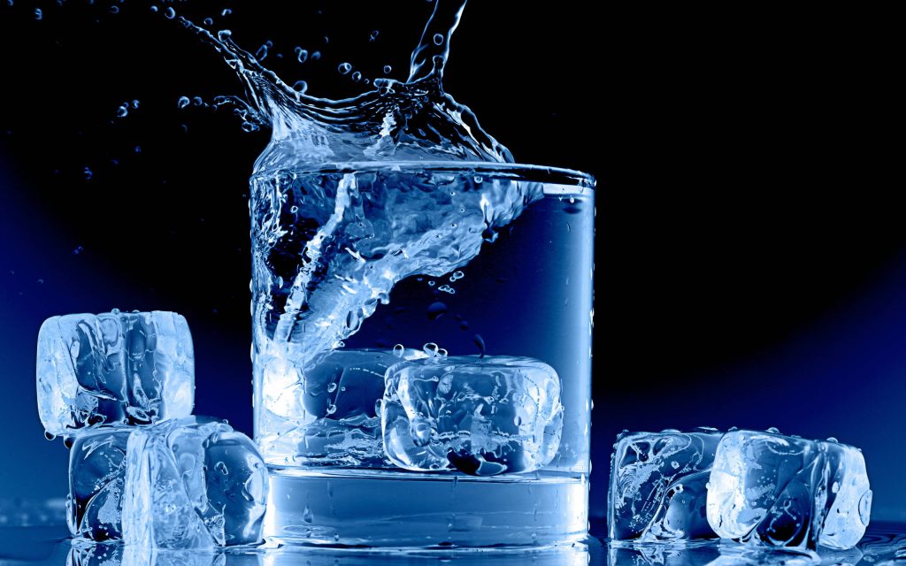 High-resolution image of a dynamic water splash in a glass with ice cubes on blue background Wallpaper