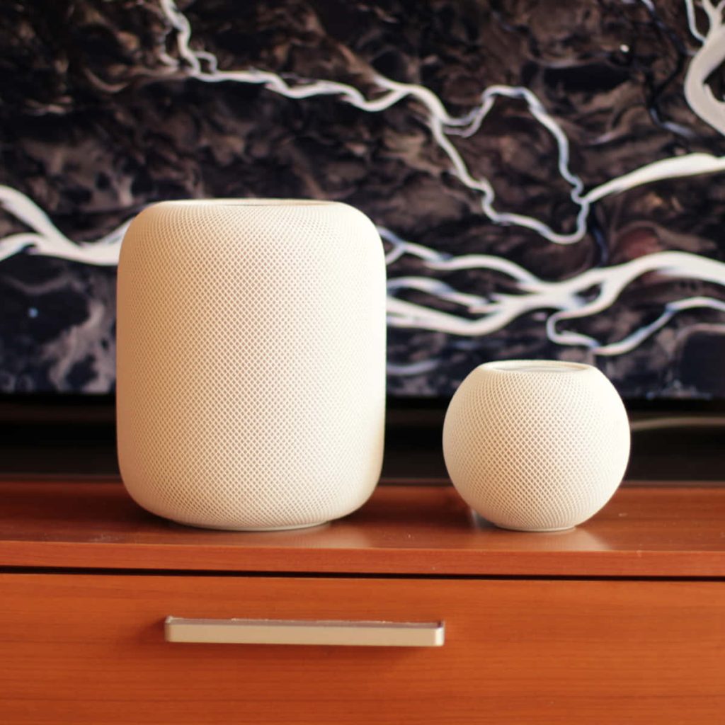 White Apple HomePod and mini smart speakers on wooden console with abstract river wallpaper background