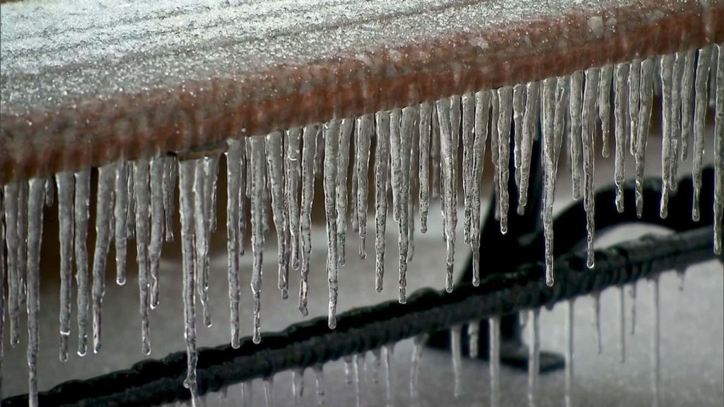 Sharp transparent icicles on a reddish outdoor railing with a soft snowy winter background wallpaper