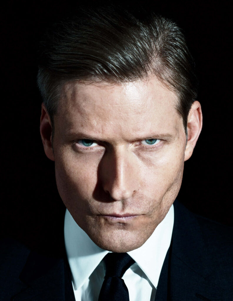 Crispin Glover portrait with intense blue eyes dramatic lighting slicked-back hair cinematic style Wallpaper